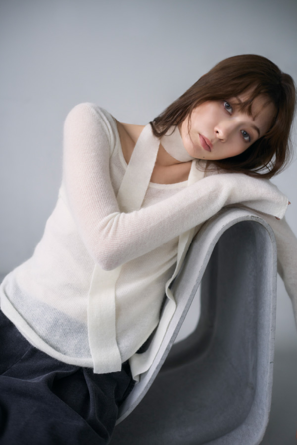 白色の後ろ開きモヘアニットとベロアカップインキャミソールを着用して椅子にもたれている女性