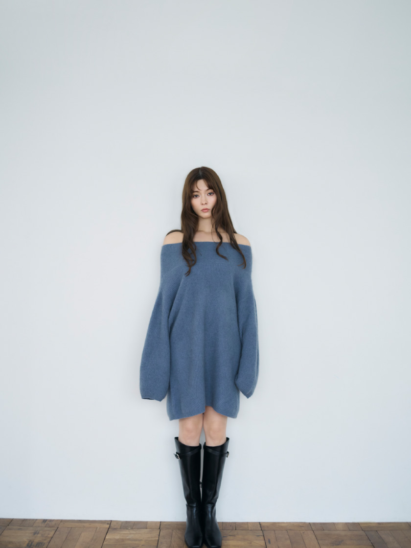 青色のラクーンニットミニワンピースと黒色のバックルストラップロングブーツを着用してる女性のモデル