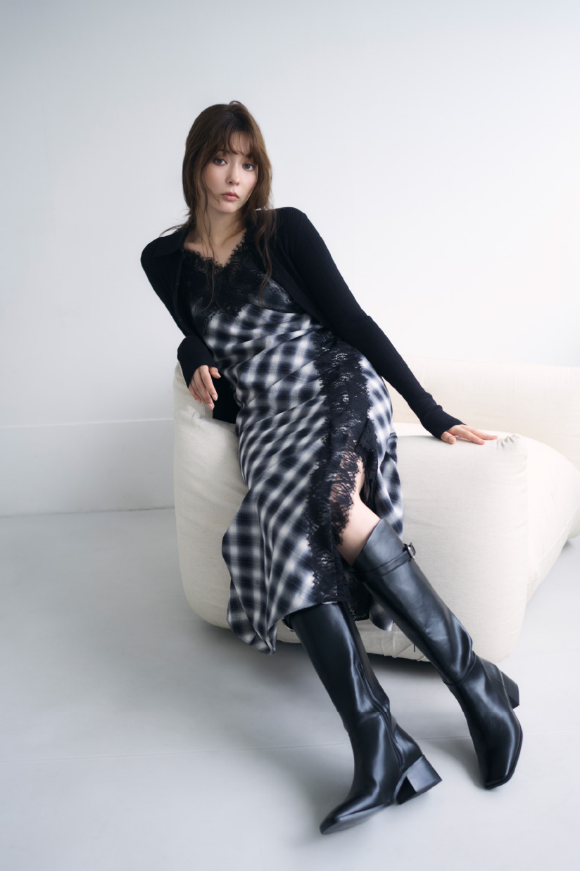 ブラック色のラメランダムリブニットポロやバックルストラップロングブーツ、レーストリムスリップドレスを着て白いソファーに座ってる女性