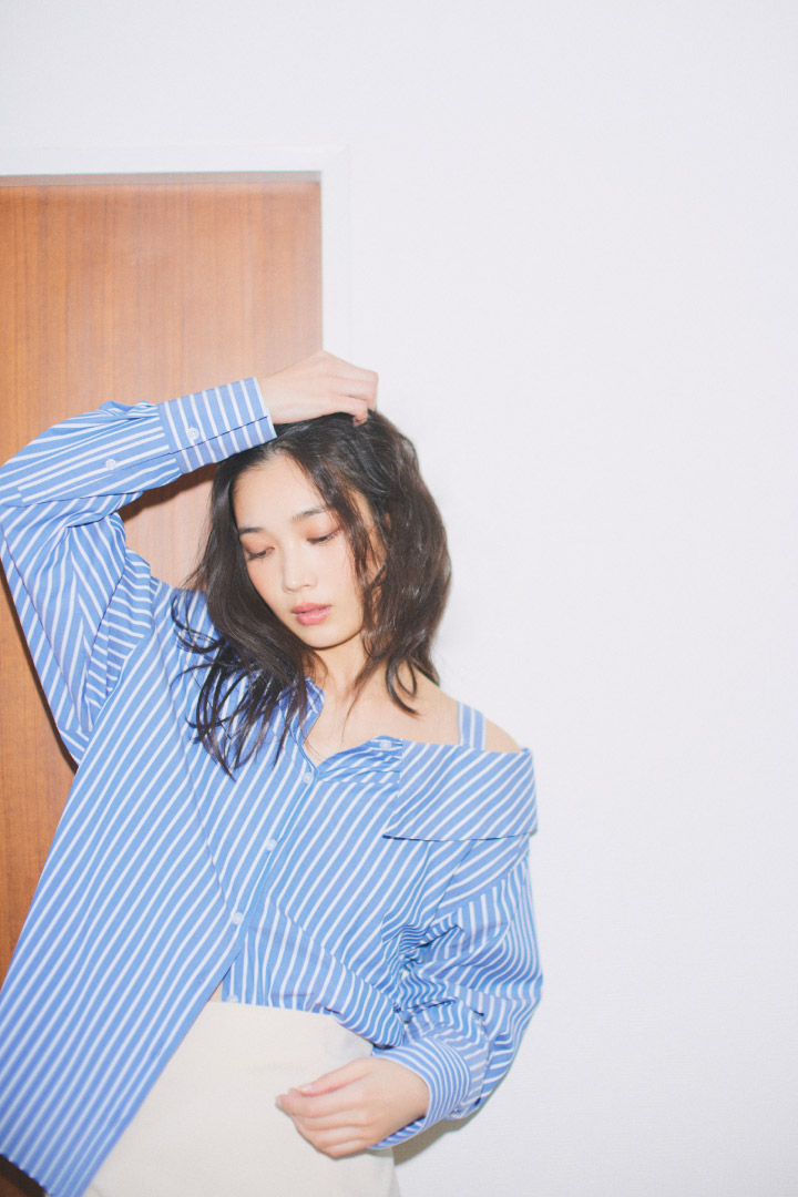 ブルーのストライプシャツ・アイボリーのスカートを履いた女性