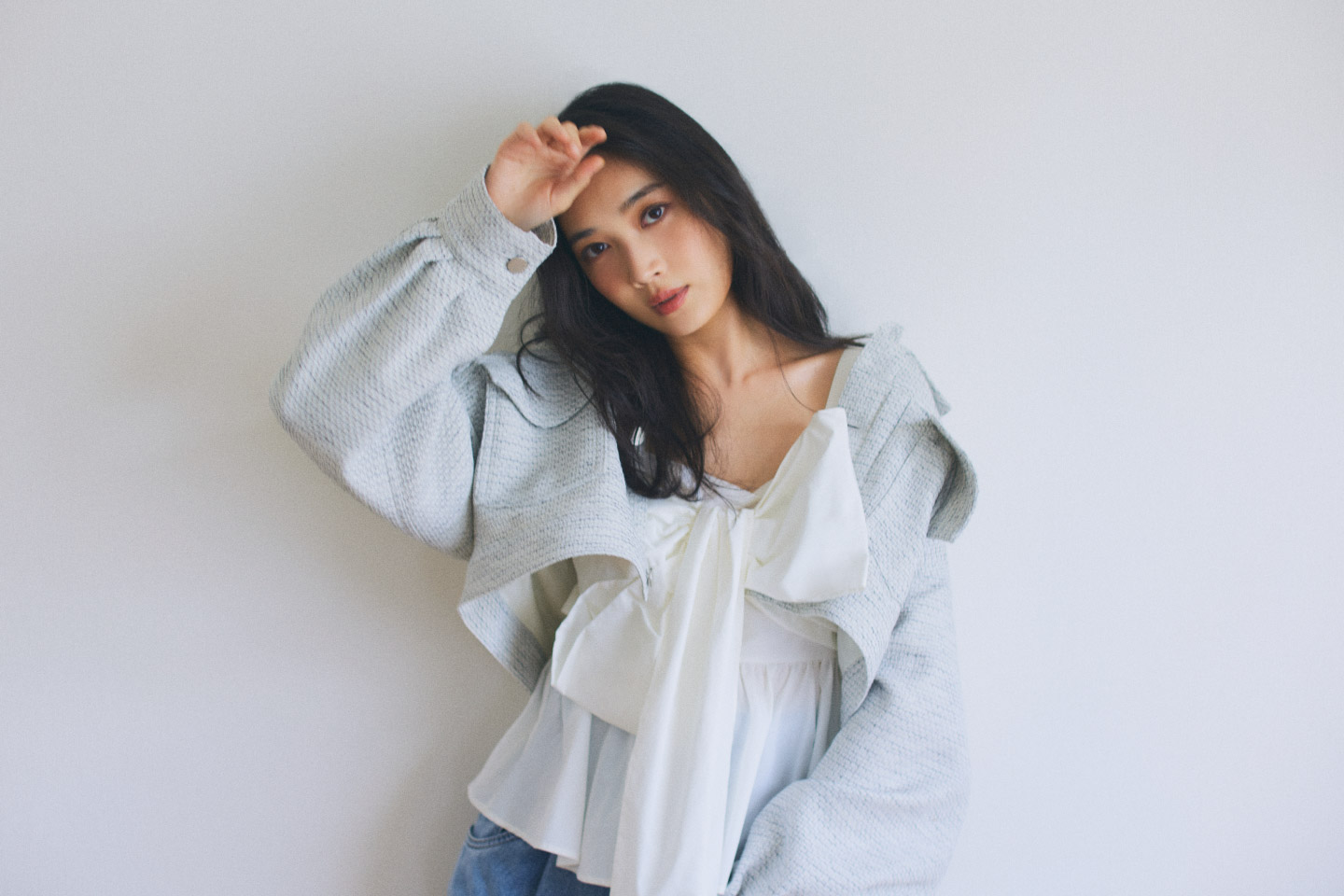 ライトグレーのジャケット・ホワイトのトップス・ブルーのデニムパンツを履いた女性