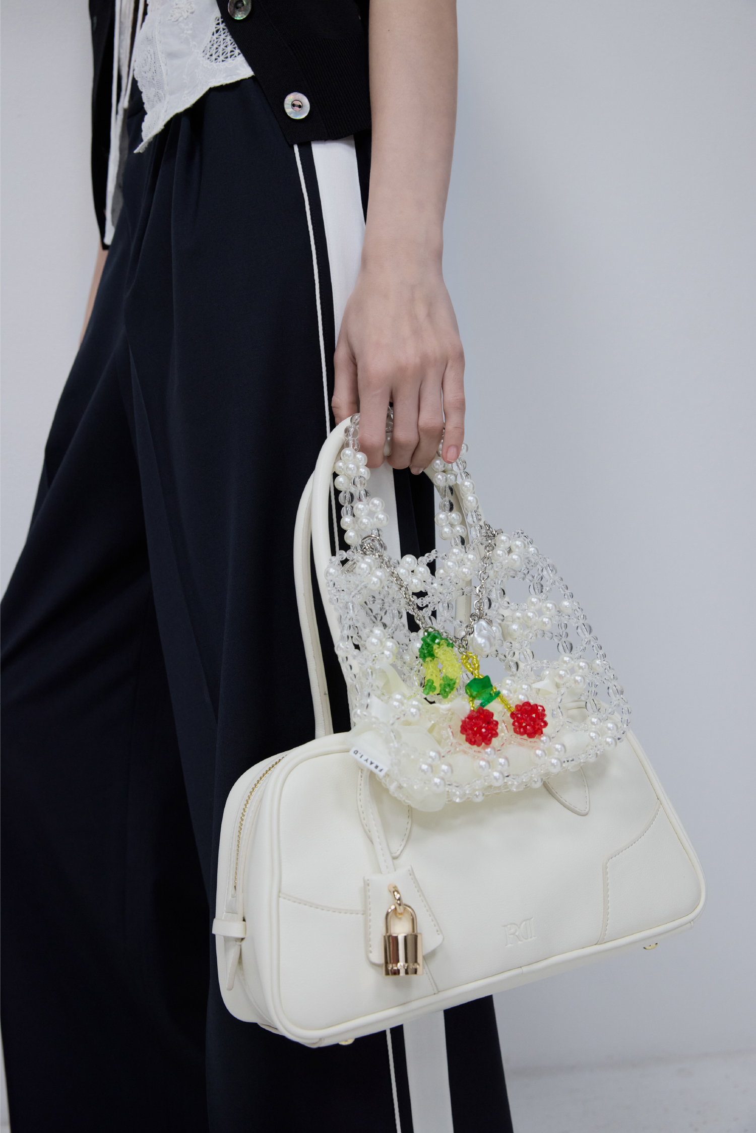 フルーツ刺繍ポロカラーノースリニットジレ&カットワークノースリーブラウス&T/Rトラックワイドパンツ&カーブィーボストンバッグ&フルーツチャーム付きビーズバック&トーションナローストラップミュールを着た女性
