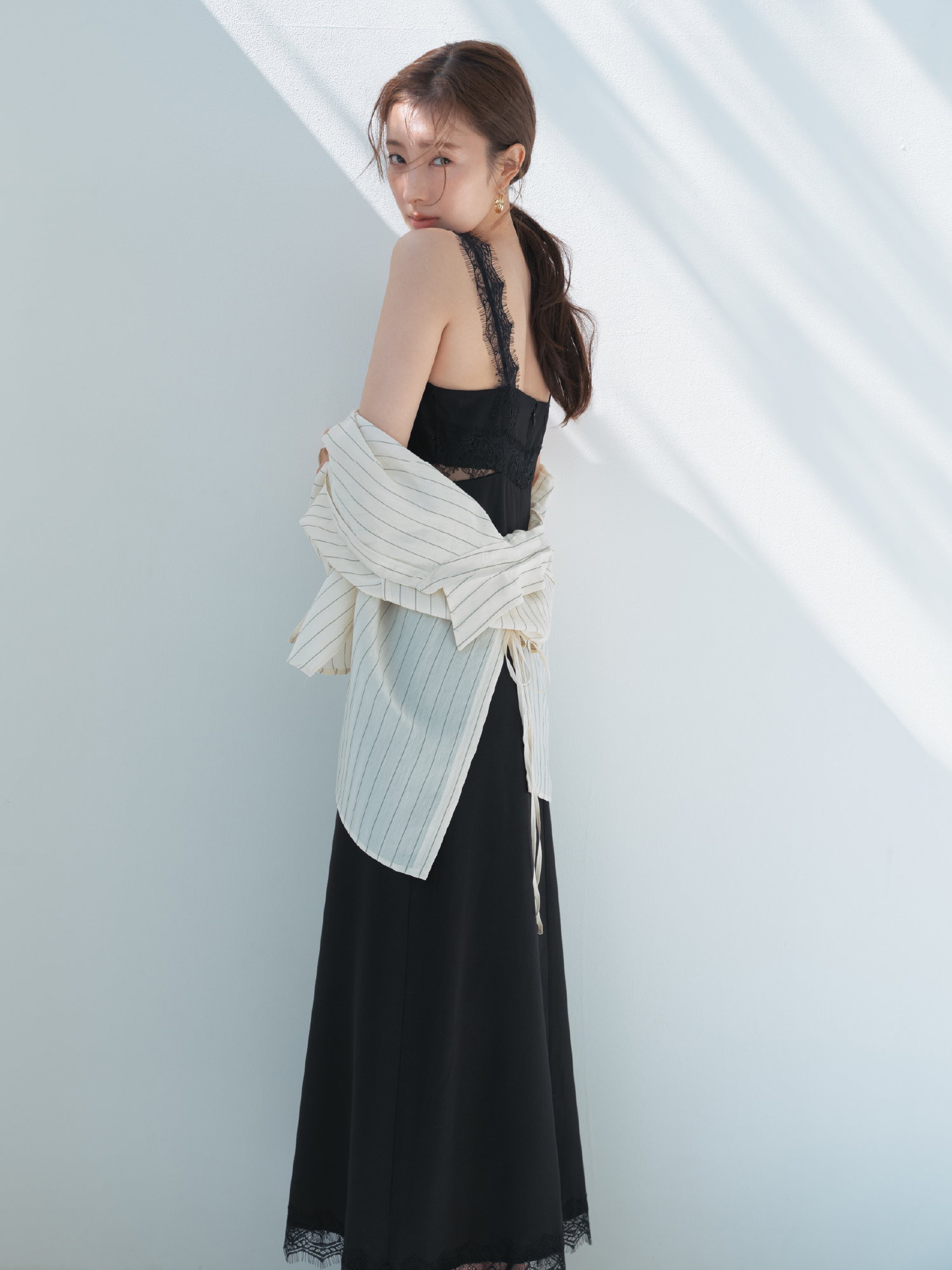 バックオープンセミシアーシャツ・サイドカッティングレーストリムキャミワンピース・クロスラインフープピアス・フラワーモチーフストラップサンダルを着用した女性