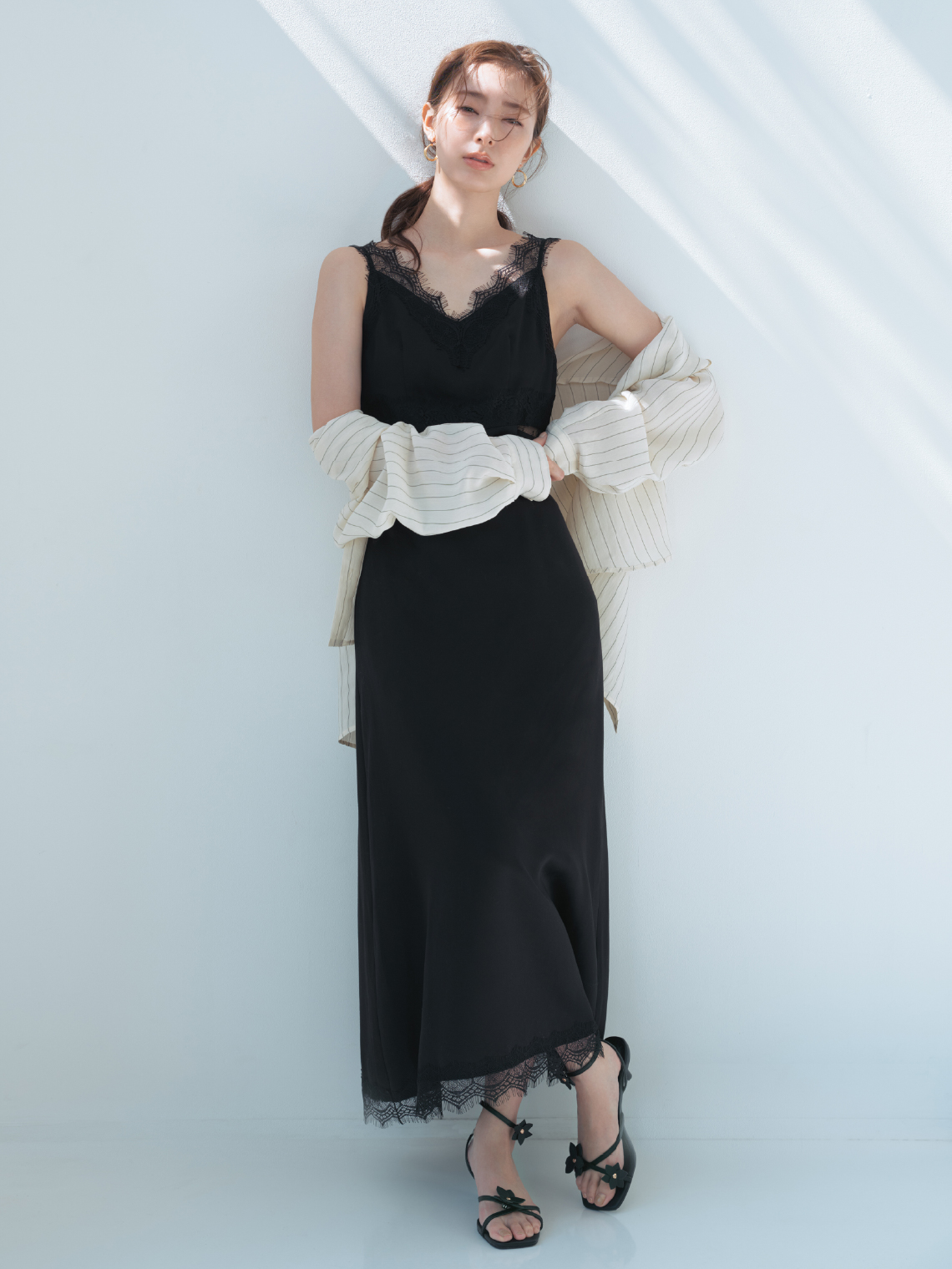 バックオープンセミシアーシャツ・サイドカッティングレーストリムキャミワンピース・クロスラインフープピアス・フラワーモチーフストラップサンダルを着用した女性