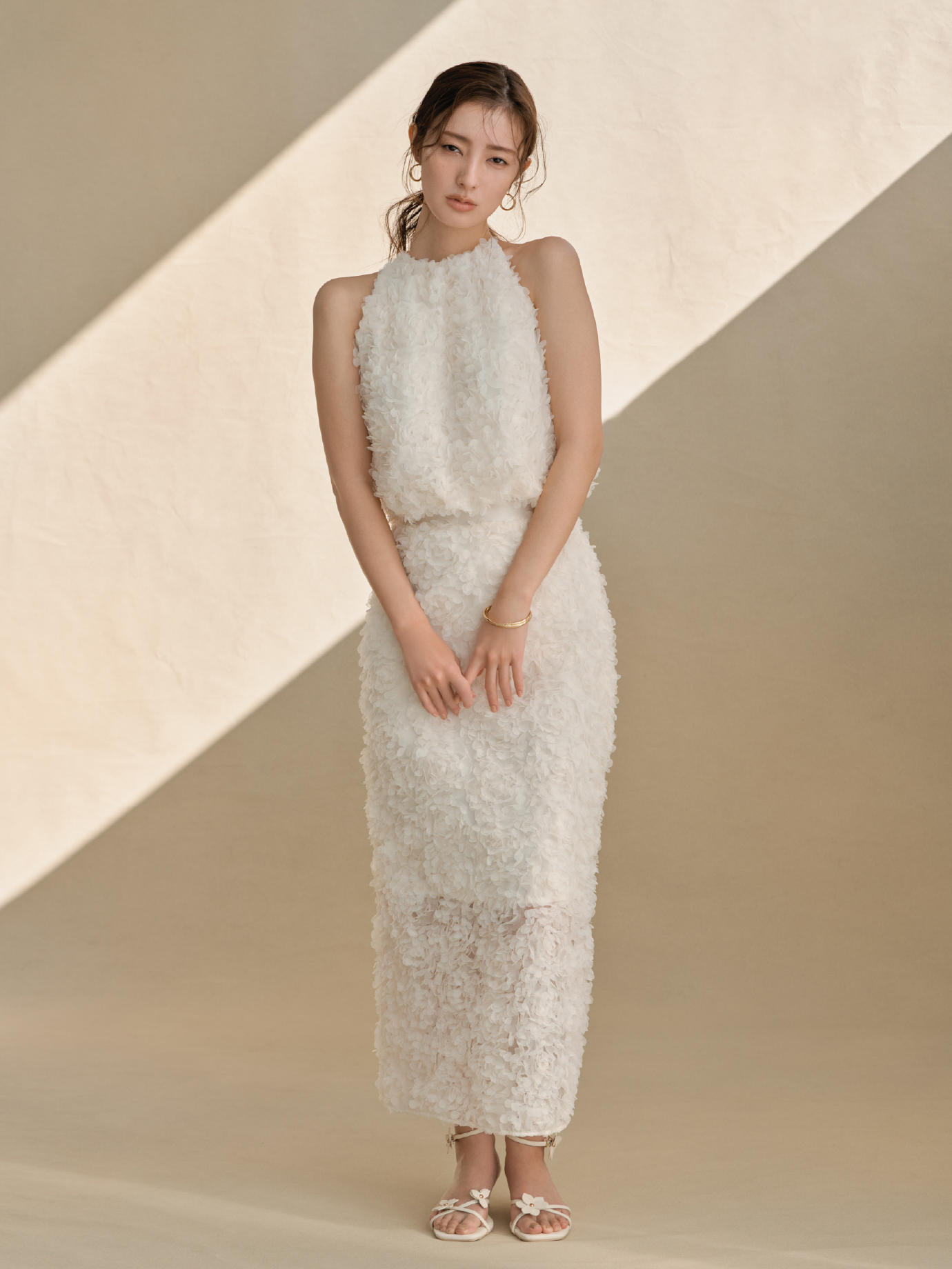 3Dフラワーホルターネックブラウス・3Dフラワーストレートスカート・クロスラインフープピアス・クロスラインバングル・フラワーモチーフストラップサンダルを着用した女性