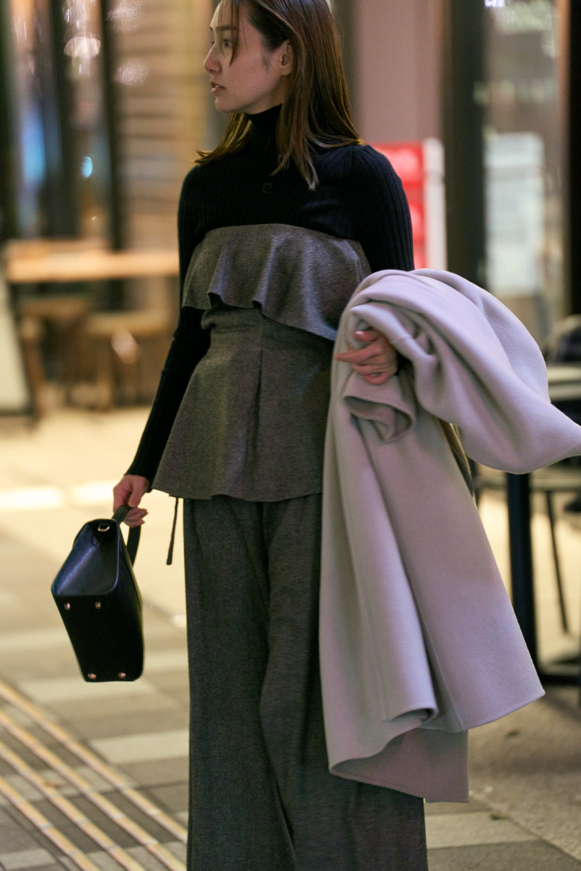 ピンクのコート・黒のトップス・グレーのパンツを履いた女性