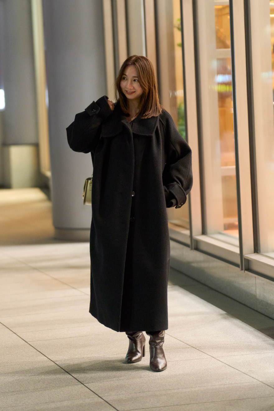 黒のコート・オフホワイトのトップス・ベージュのミニスカート・黒のロングブーツを履いた女性