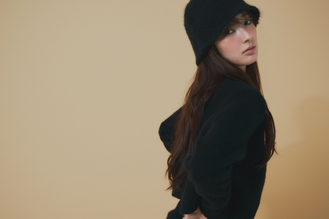 ブラックのキャップ・ブラックのセットアップ・ベージュのジャケットを着用した女性
