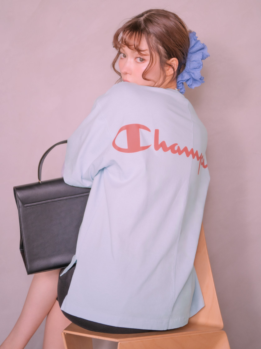 青色の【Champion】レイヤードロンＴとロゴチャームカットワークシュシュ、ブラック色のナローベルトワンハンドルバッグを持って椅子に座ってる女性のイメージ