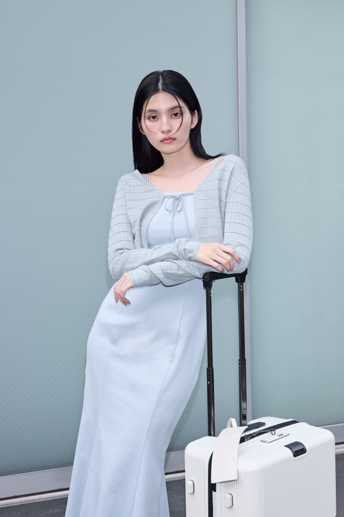 アイボリー色の【Samsonite】コラボスーツケースを持ちライトブルー色のシルクブレンドタックブロッキングアンサンブルニットとカップインマーメイドカットキャミＯＰを着てる女性のイメージ