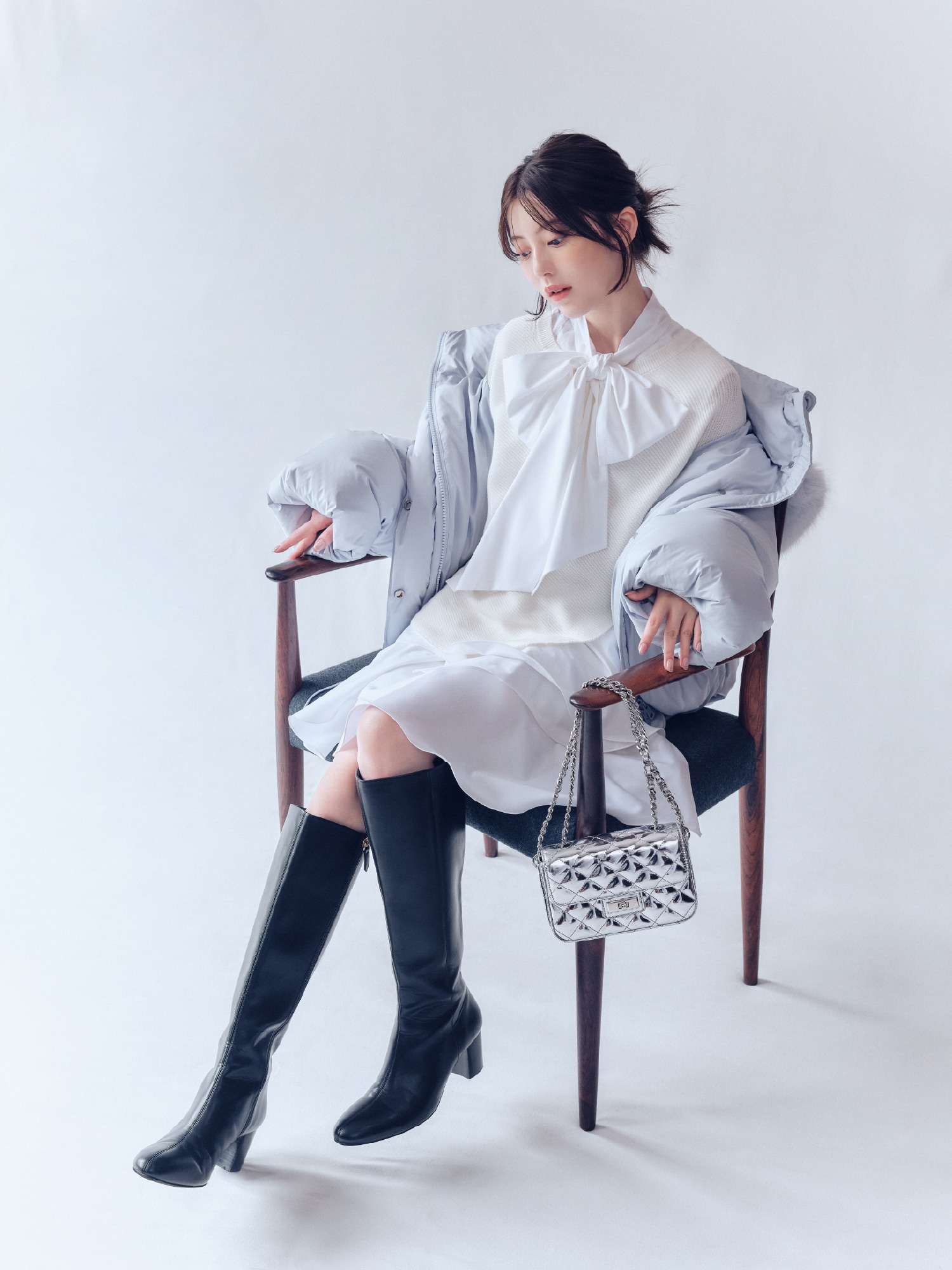 ライトブルーのフードファーショートダウンコートと白リボンタイチュニックコンビニットとメタリックチェーンバッグと黒ラウンドトゥロングブーツの着用例