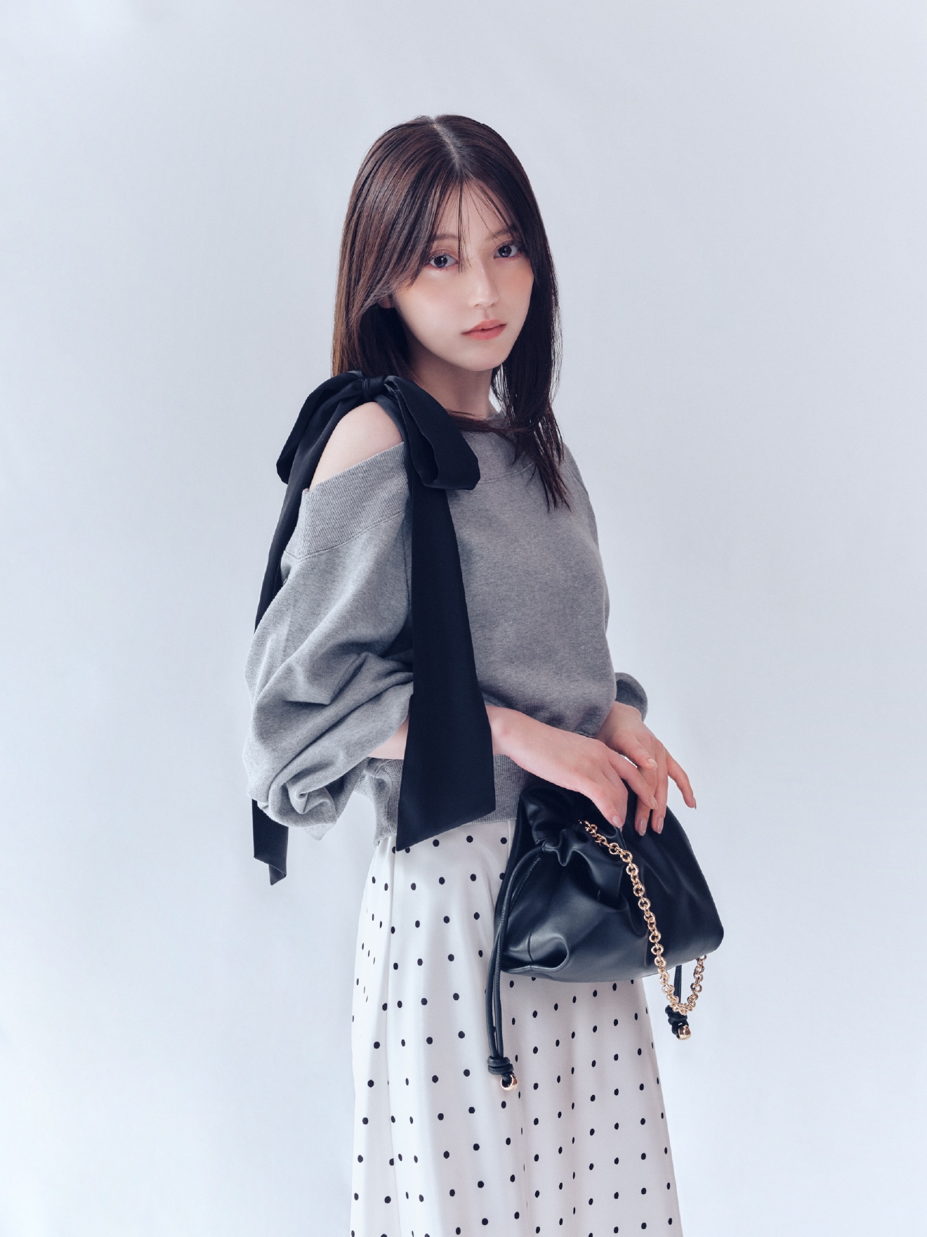 グレーのビッグリボンワンショルカットソーと白地にドット柄のハイウエストサテンナロースカート、黒のノットドローストリングバックの着用例