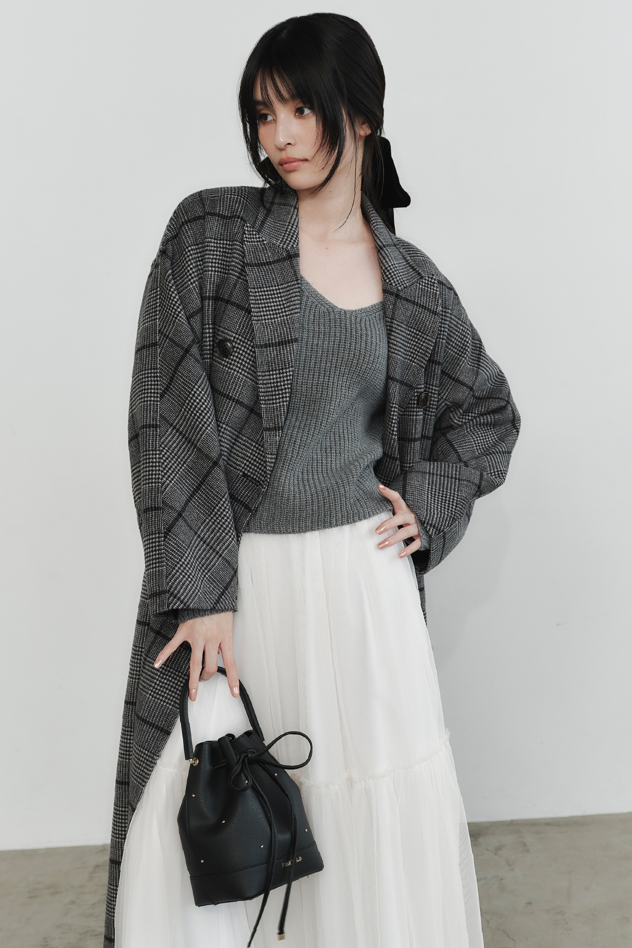 ウールリバーダブルブレストピークドチェスターコート・リボンニットプル＆チュールスカートセット・ドローストーリングスタッズリボンバッグ・キトゥンヒールロングブーツを着用した女性の画像