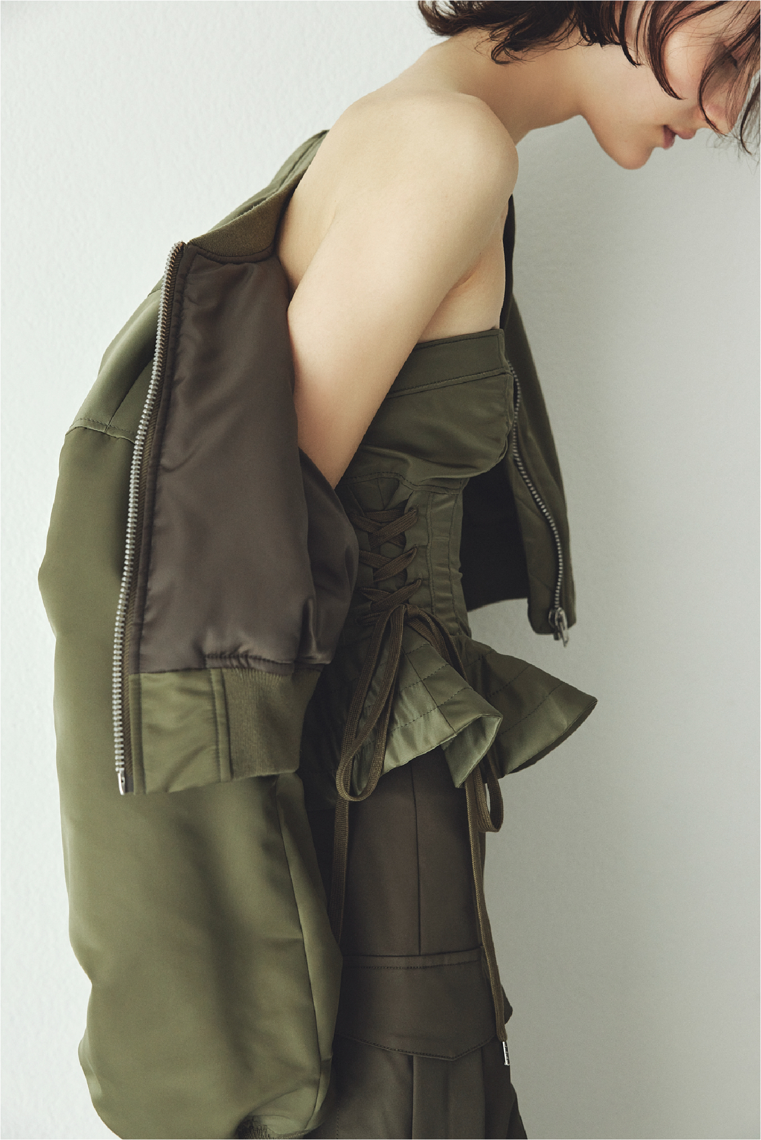 レースアップショートMA-1・レースアップビスチェ・イレヘムミリタリースカート・クリアヒールサンダルを着用した女性の画像