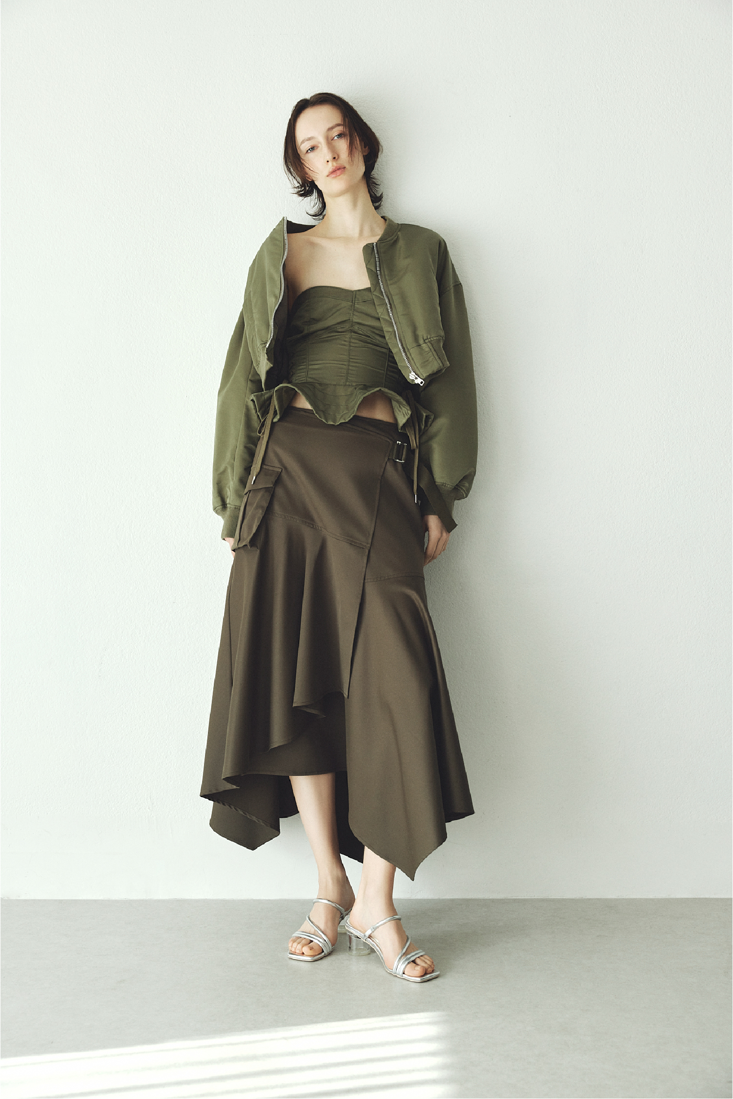 レースアップショートMA-1・レースアップビスチェ・イレヘムミリタリースカート・クリアヒールサンダルを着用した女性の画像