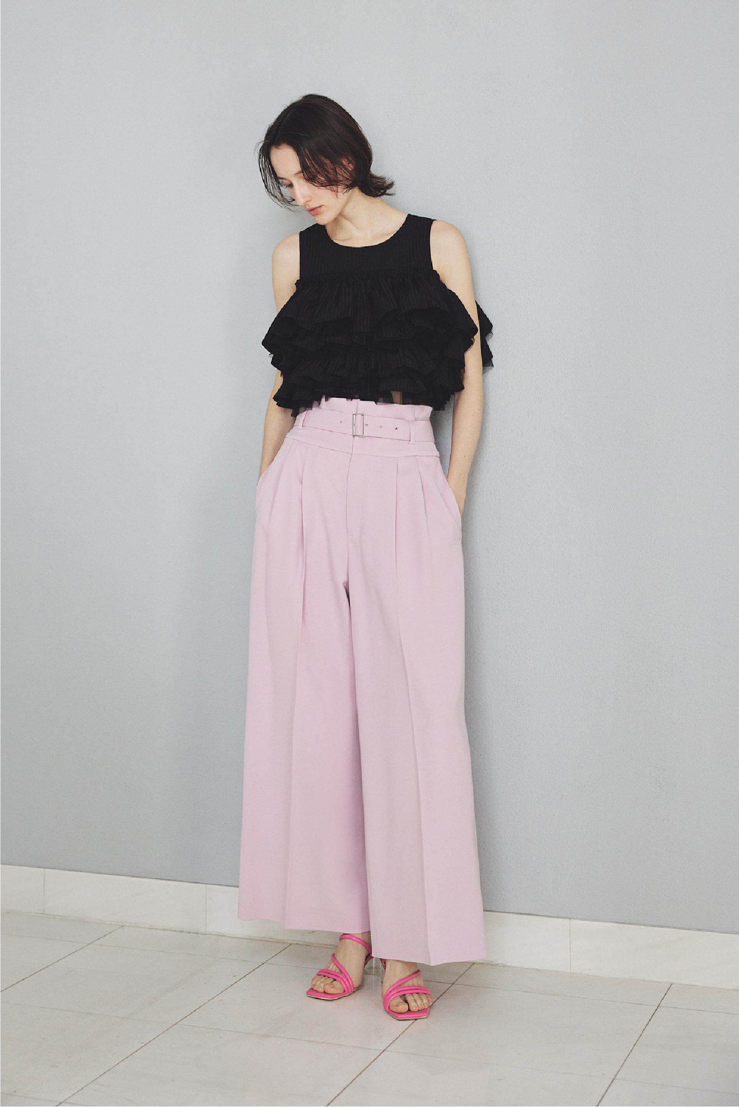 チュールコンビフリルティアードブラウス・ハイウエストベルトパンツ・クリアヒールサンダルを着用した女性の画像